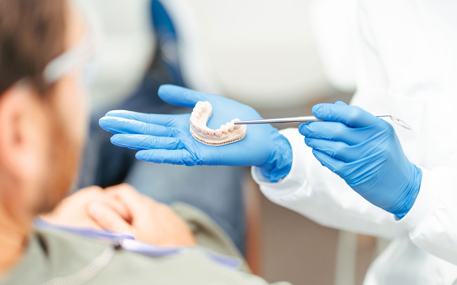 Dentist holding a dental mold, pointing with a tool, in front of a patient.