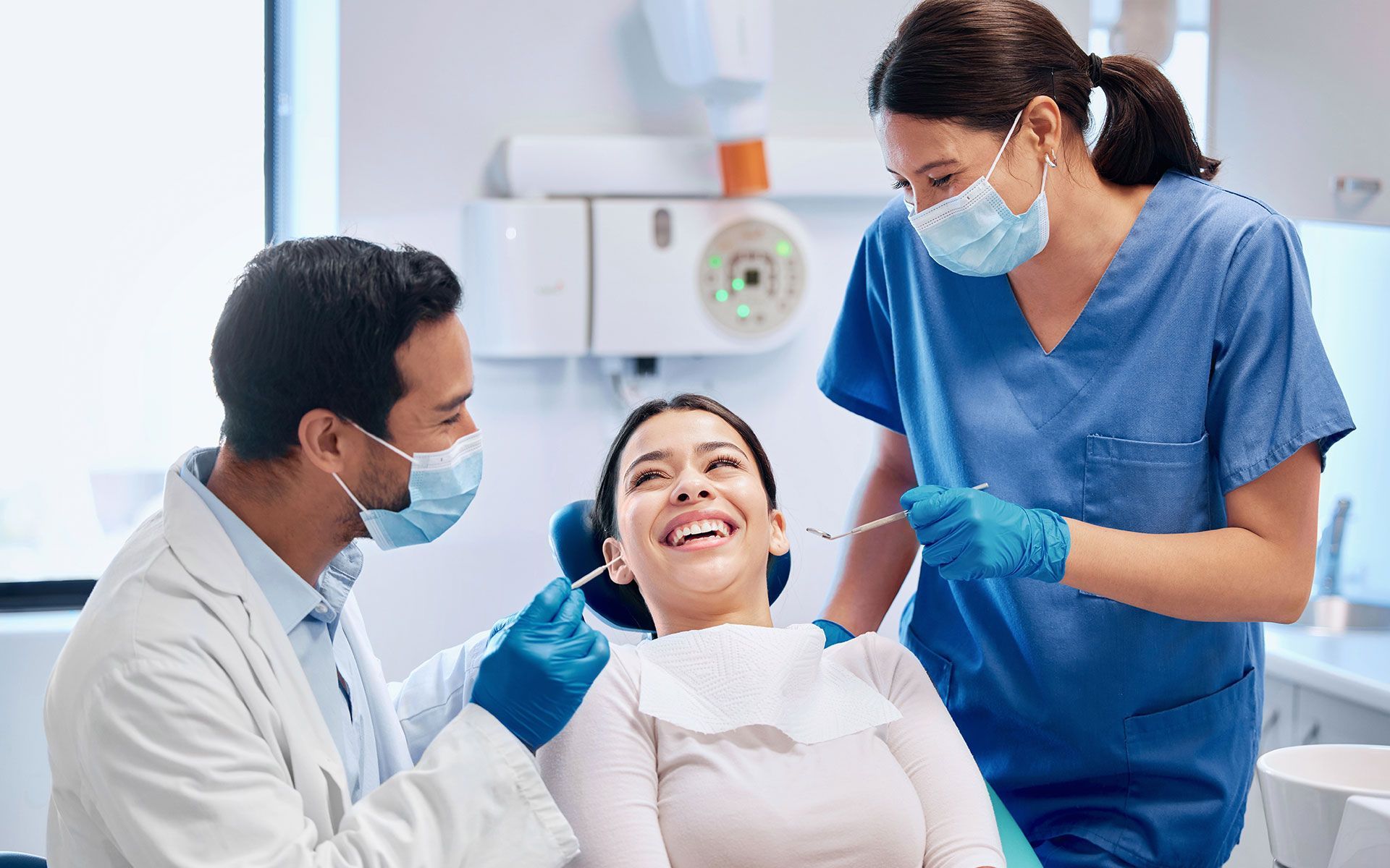 Dentist and assistant examining a smiling patient in a dental office.