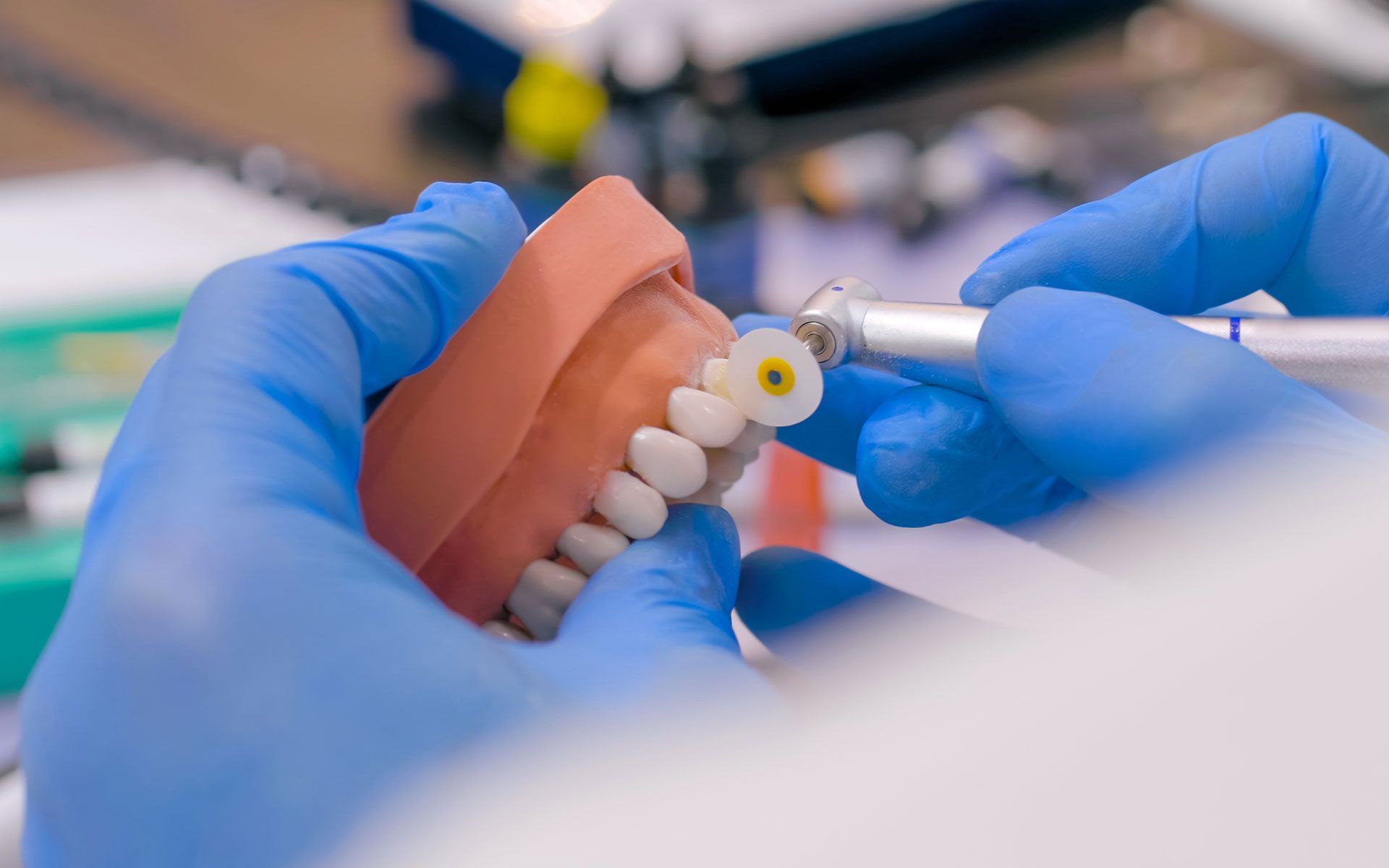 Hands in blue gloves working on dental model with a drill.