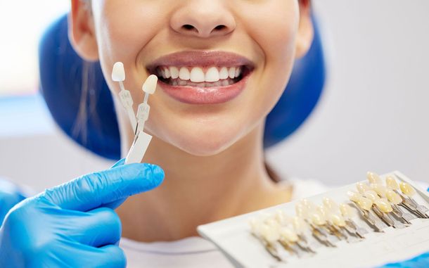 Woman smiling with dental shades in front of teeth, dentist in blue gloves.