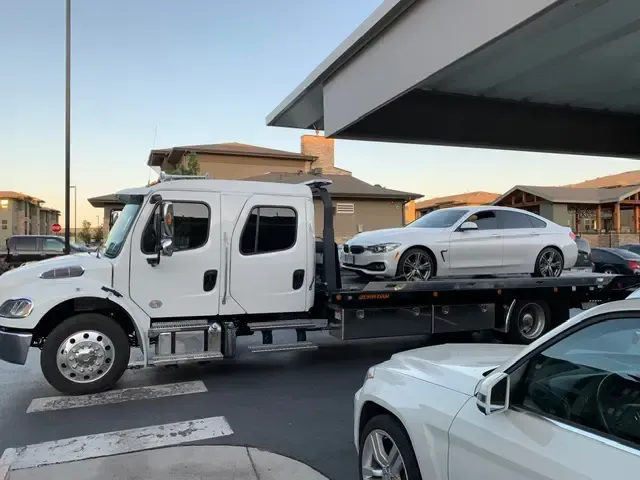 A tow truck with a white car on the back of it
