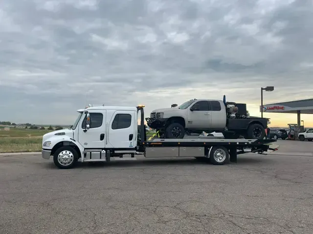 A tow truck is carrying a truck on the back of it.