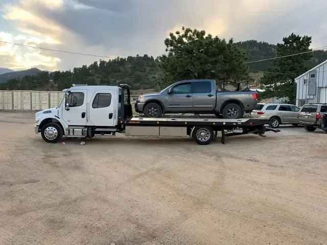 A tow truck is carrying a truck on the back of it.