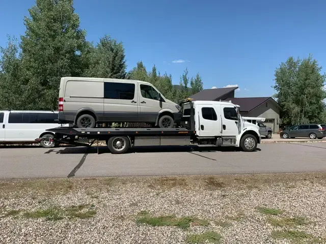A tow truck is carrying a van on the back of it.