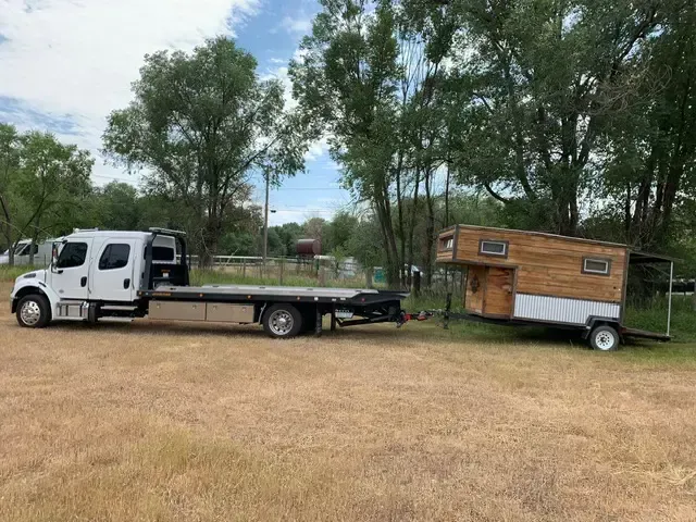 A tow truck is towing a tiny house on a trailer.