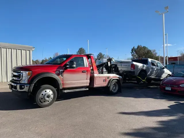 A red tow truck is towing a car in a parking lot.