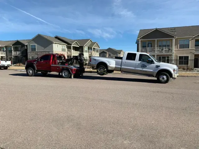 A red truck is being towed by a white truck.