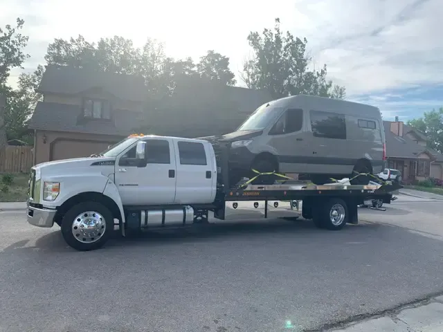 A tow truck is towing a van down a street.