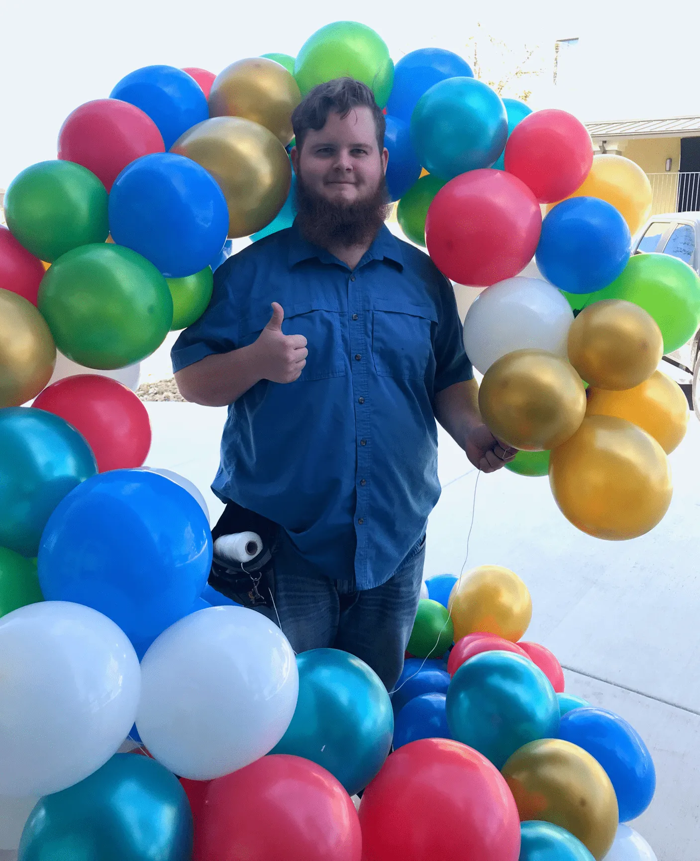 a man with a beard is standing in front of a bunch of balloons and giving a thumbs up