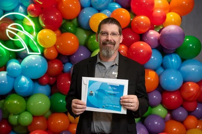 a man is holding a certificate in front of a wall of balloons