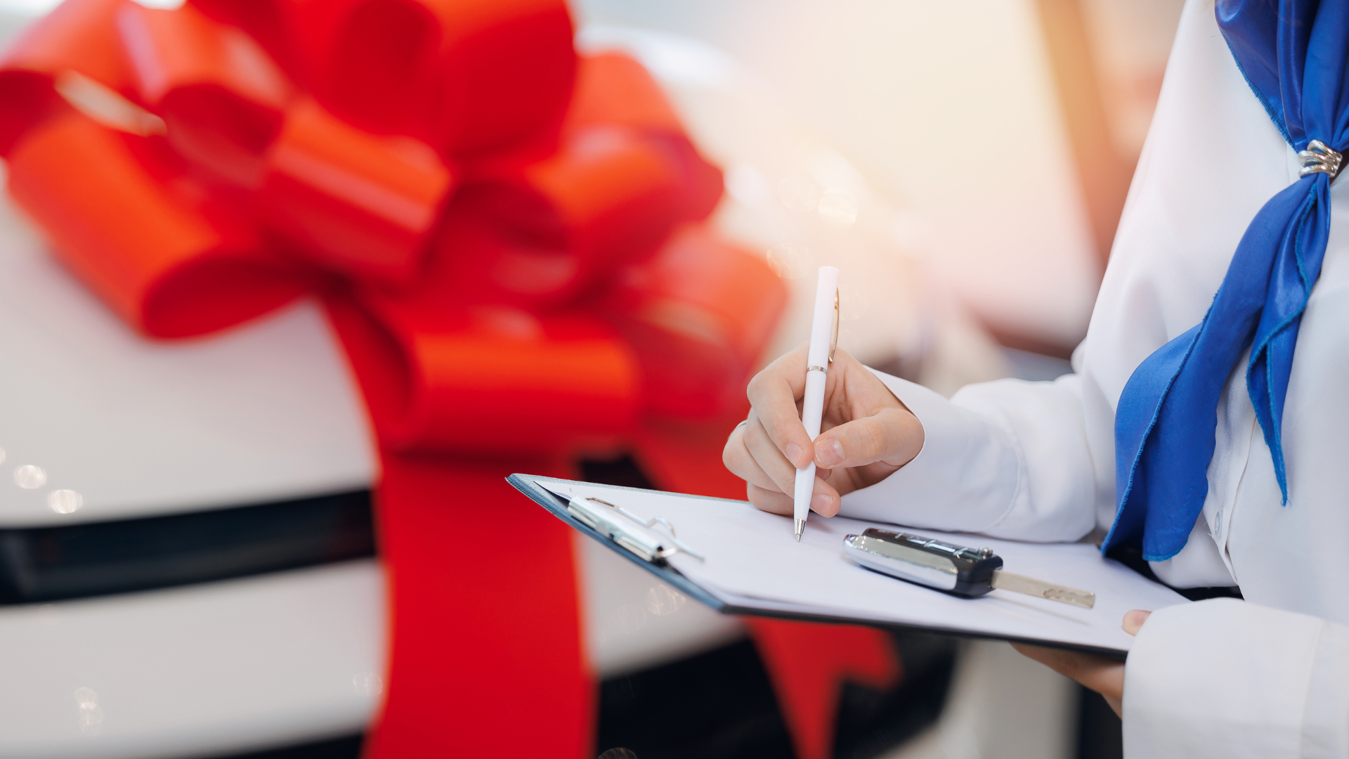 A woman is writing on a clipboard in front of a car with a red bow.