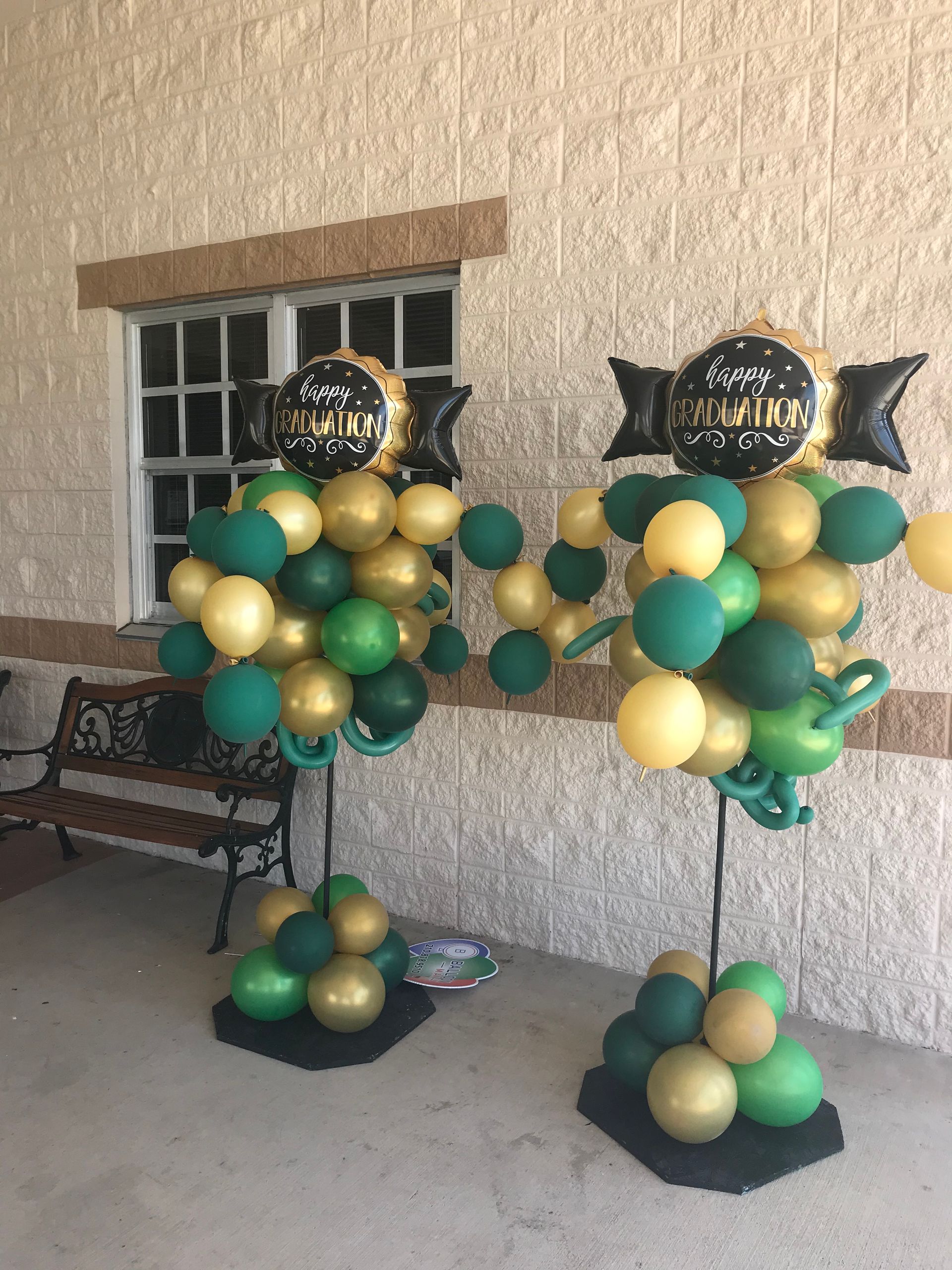 Two graduation balloon columns in gold and green balloons are placed outside.