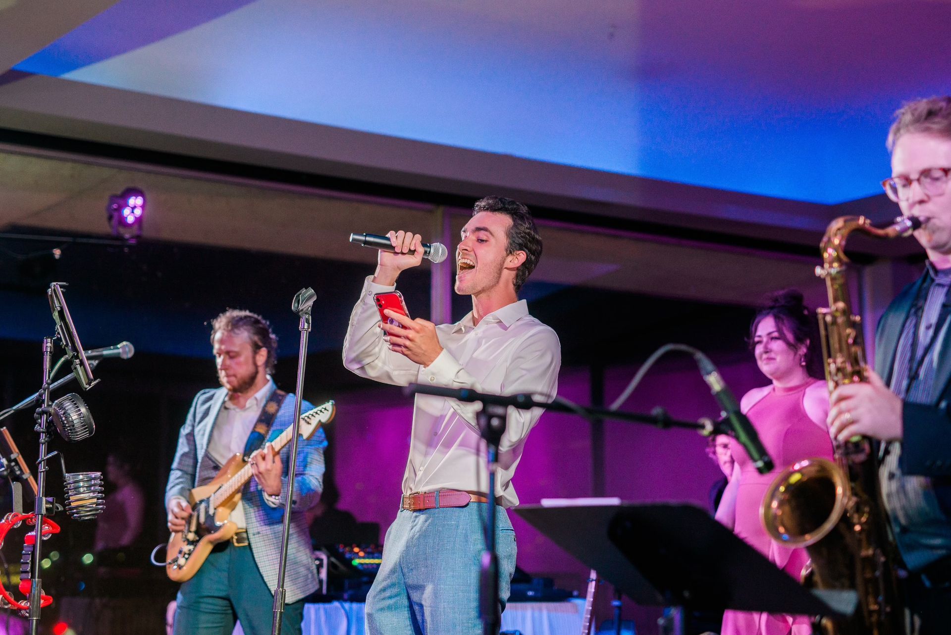 A man is singing into a microphone while playing a guitar and a saxophone.