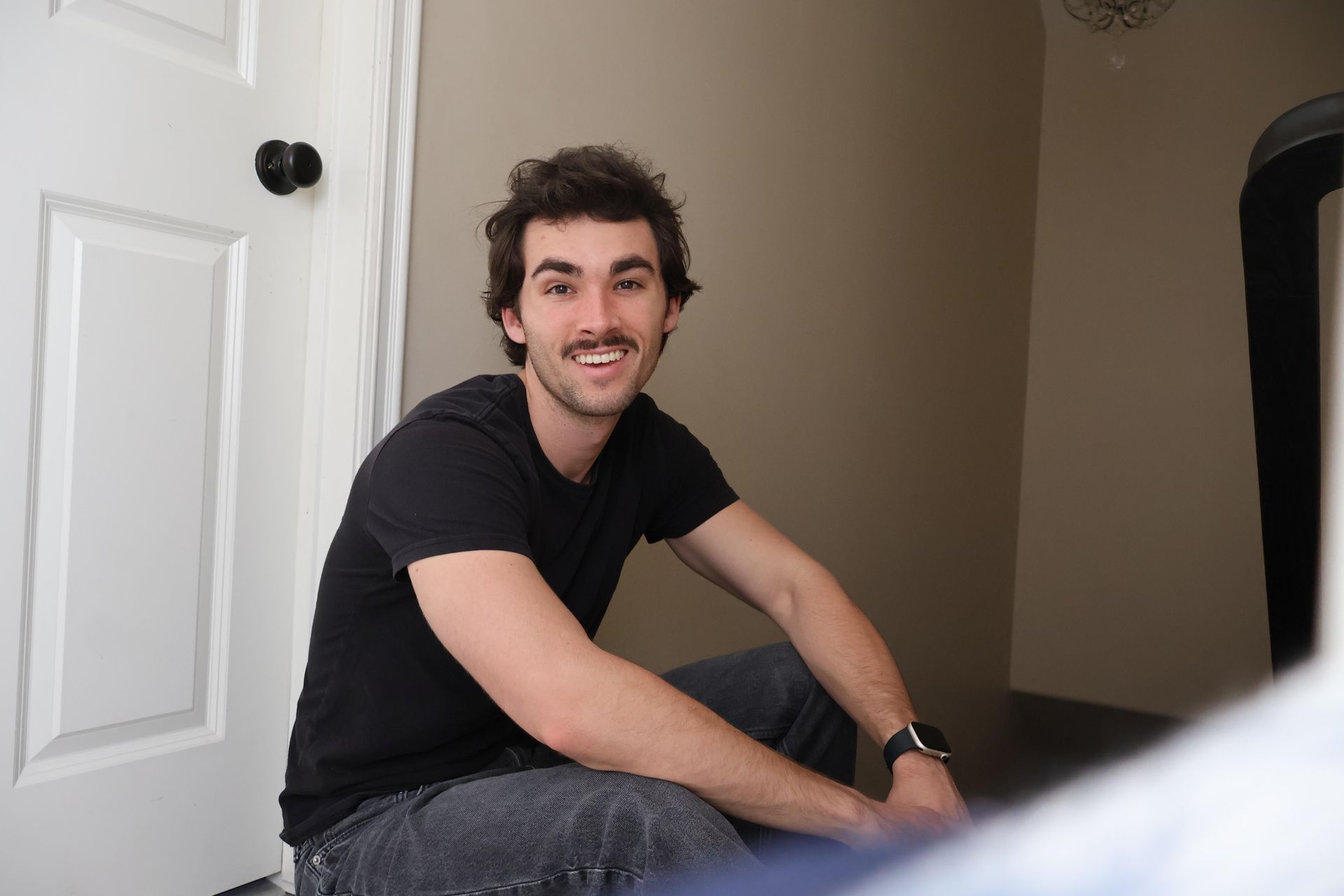 A man with a mustache is sitting on the floor in front of a door.