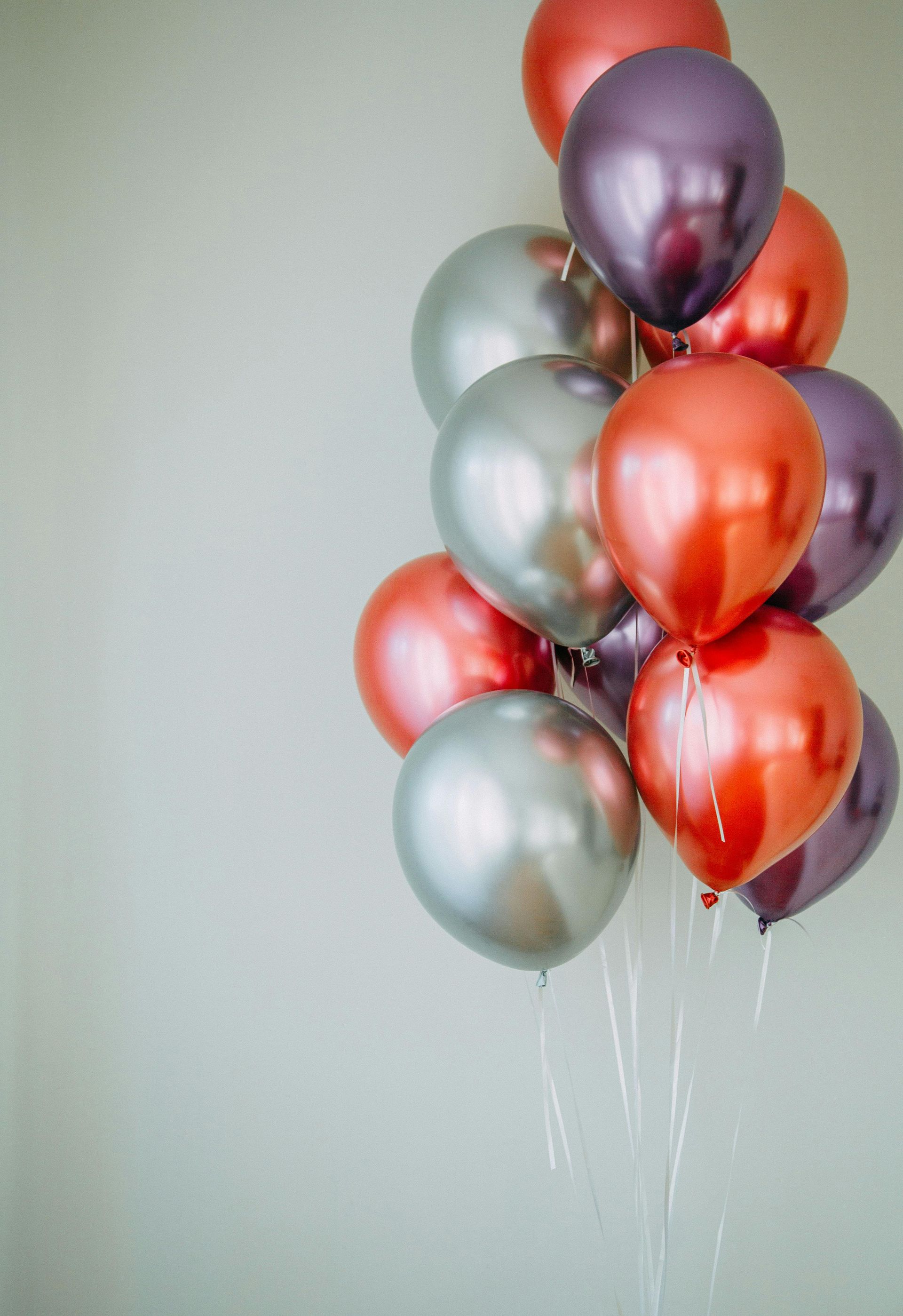A bunch of red , silver and purple balloons hanging from a string.