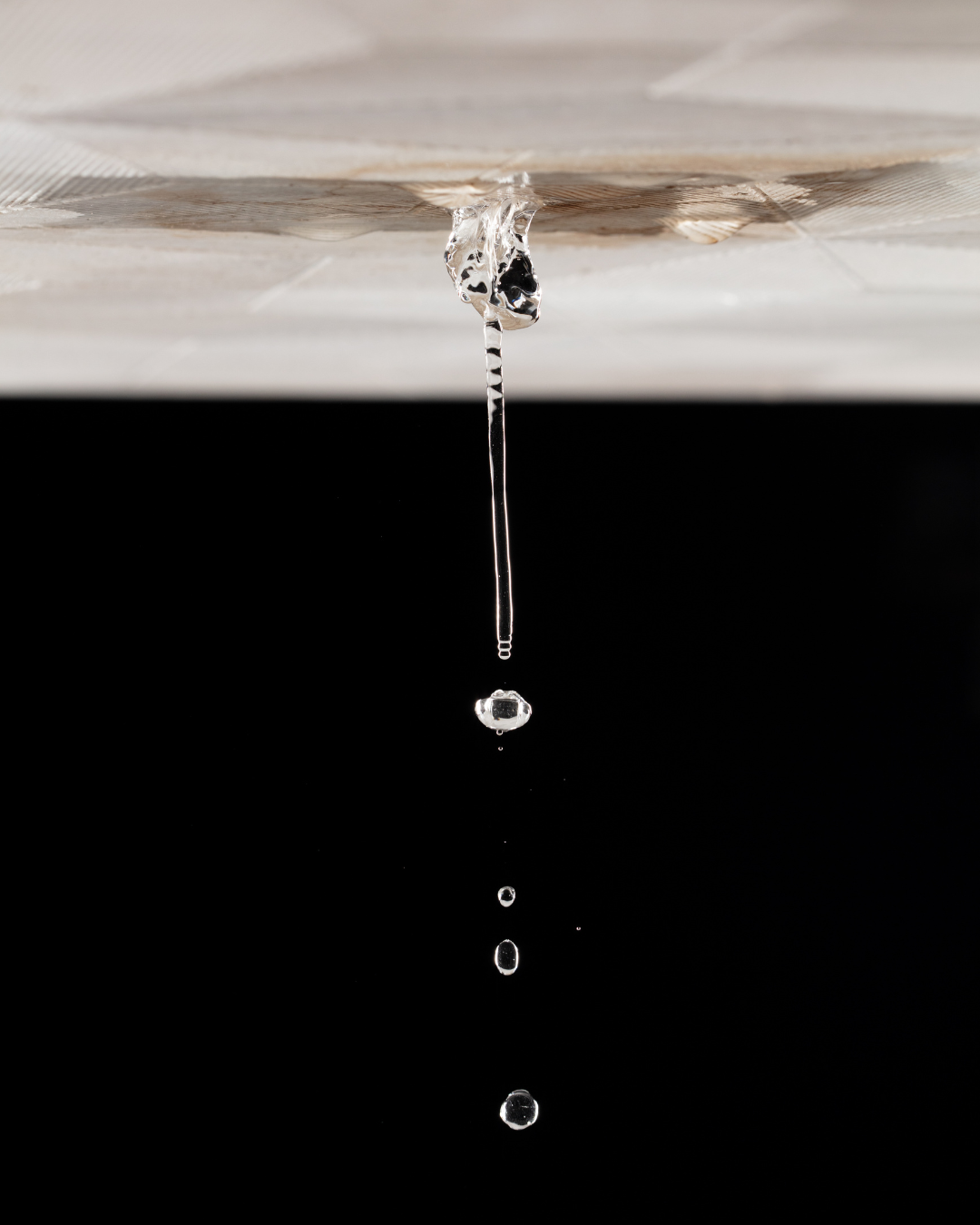 A close-up view of a ceiling leak with water dripping steadily downward. The damaged ceiling shows m