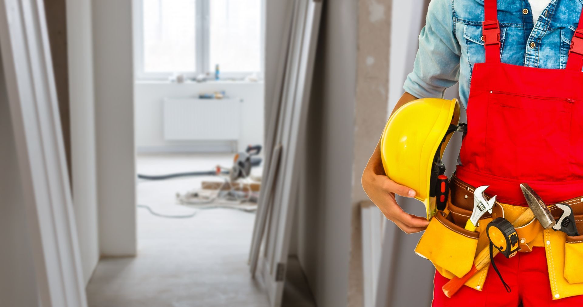 Un operaio edile tiene in mano un casco e una cintura portautensili.