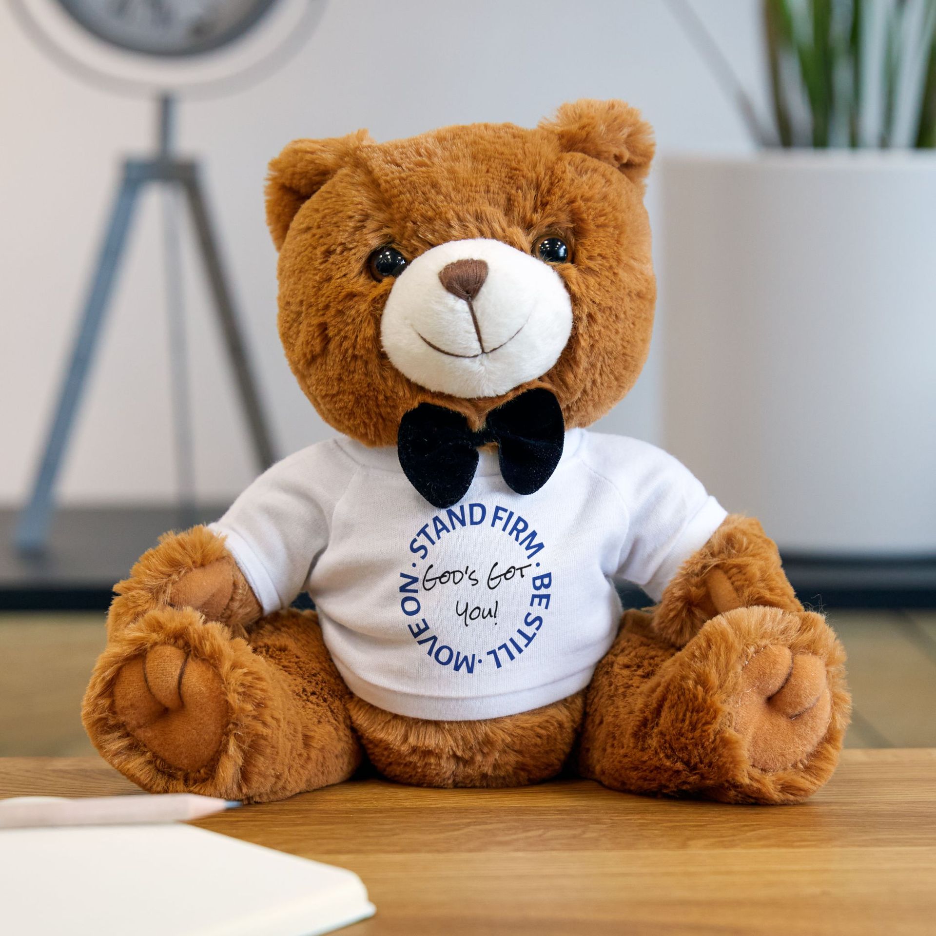 Brown teddy bear with a black bow tie, wearing a white shirt that says,