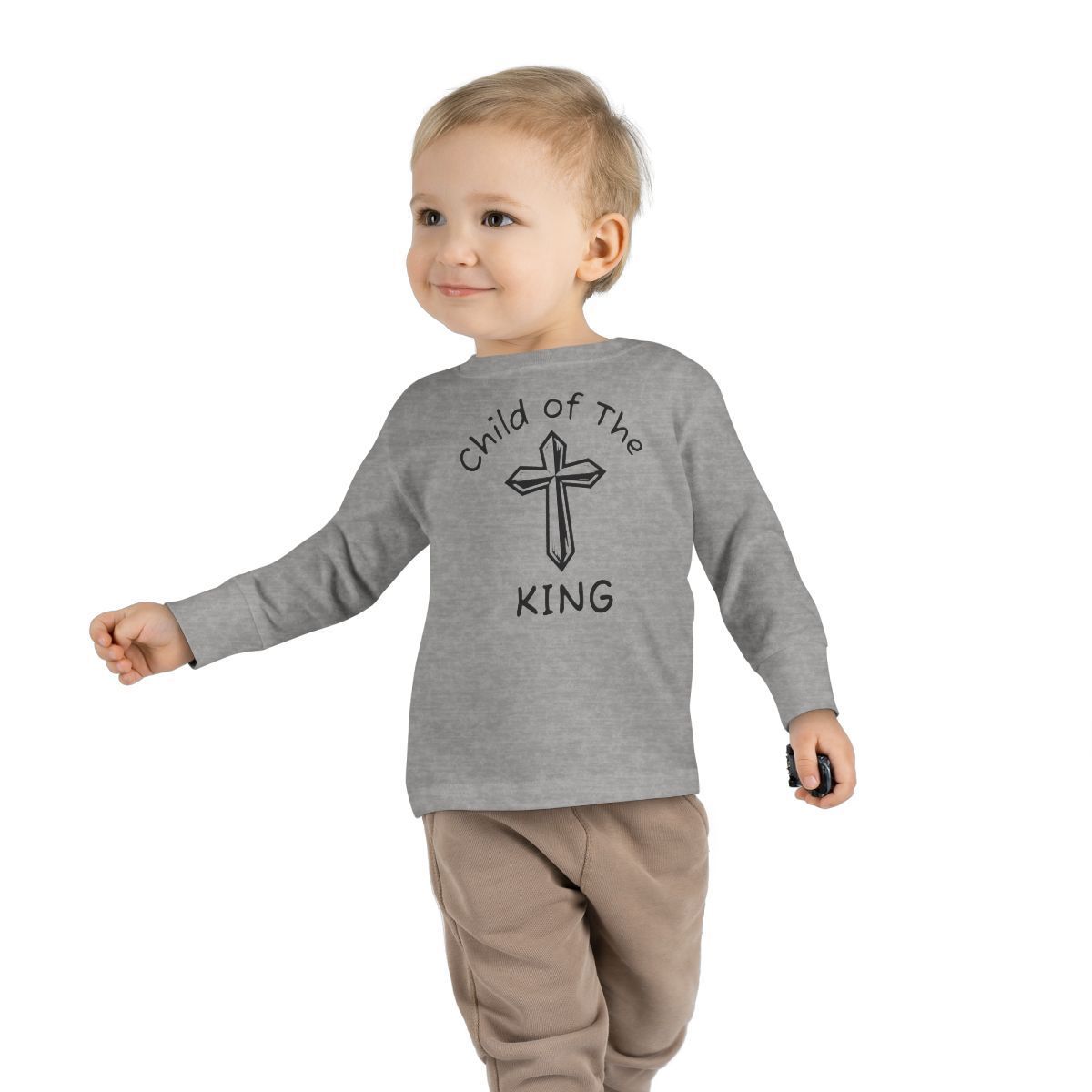 A toddler wearing a gray long-sleeve shirt with a cross and the text