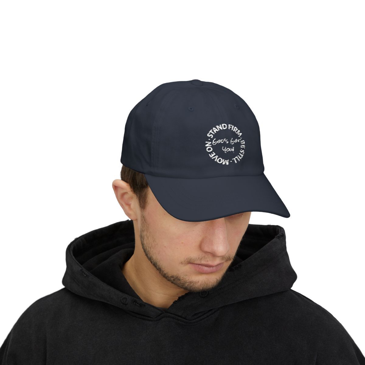 Man wearing a navy blue baseball cap with white text inside a circle on a black hooded sweatshirt.