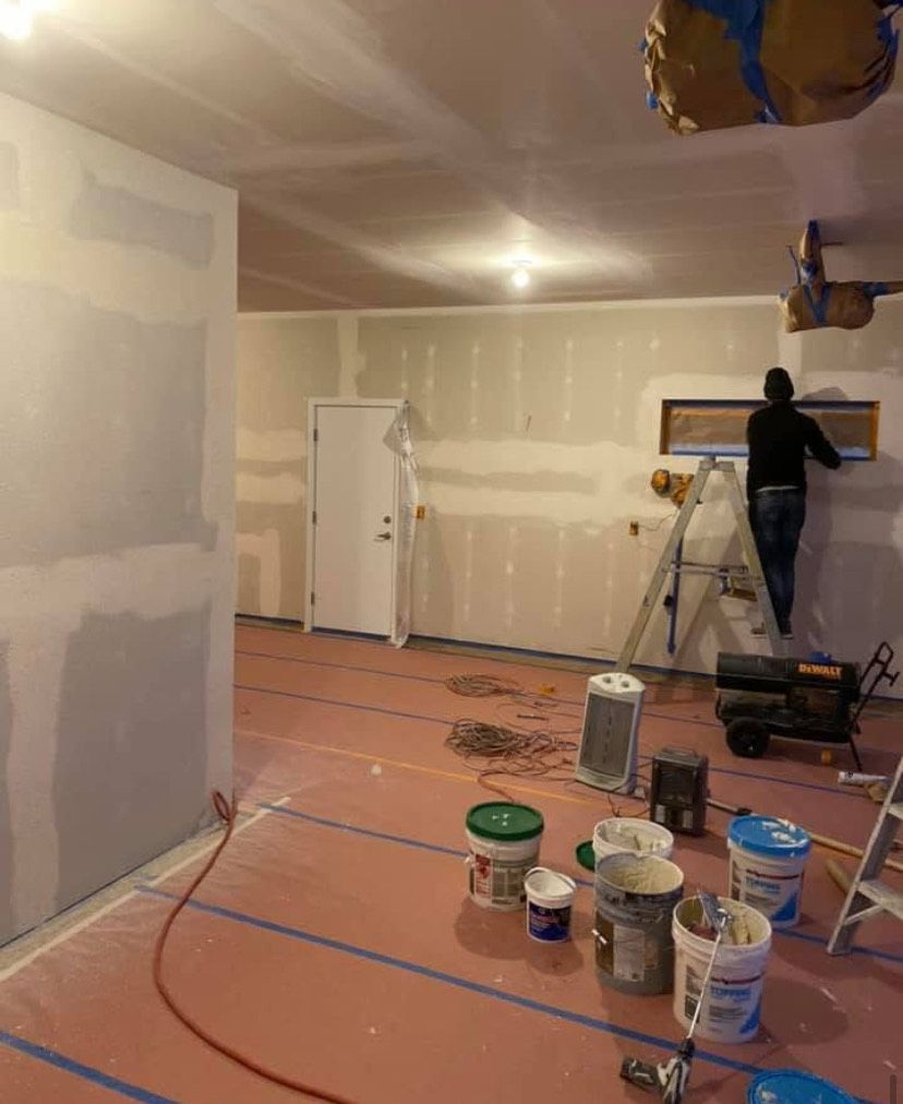 Person painting a drywall-renovated room with buckets and tools on the floor.