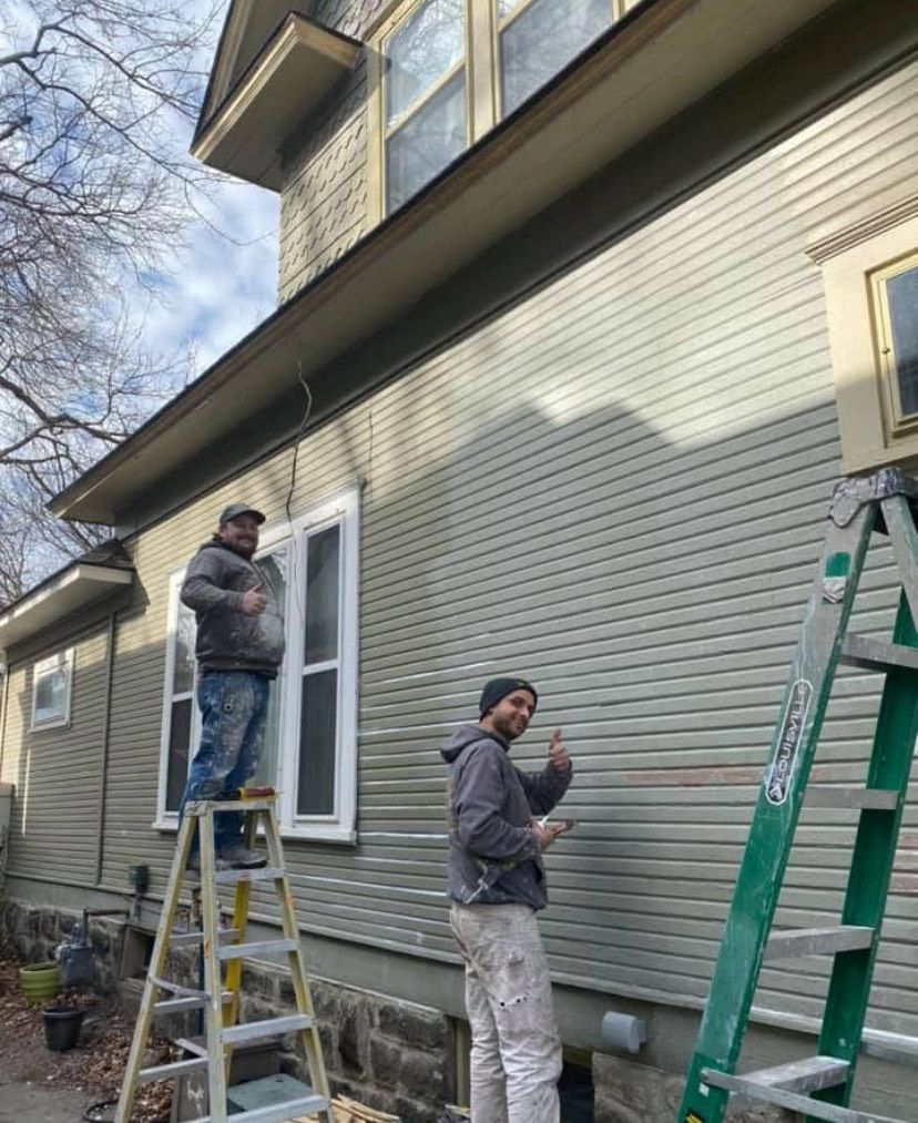 Two workers on ladders painting a beige house exterior on a sunny day