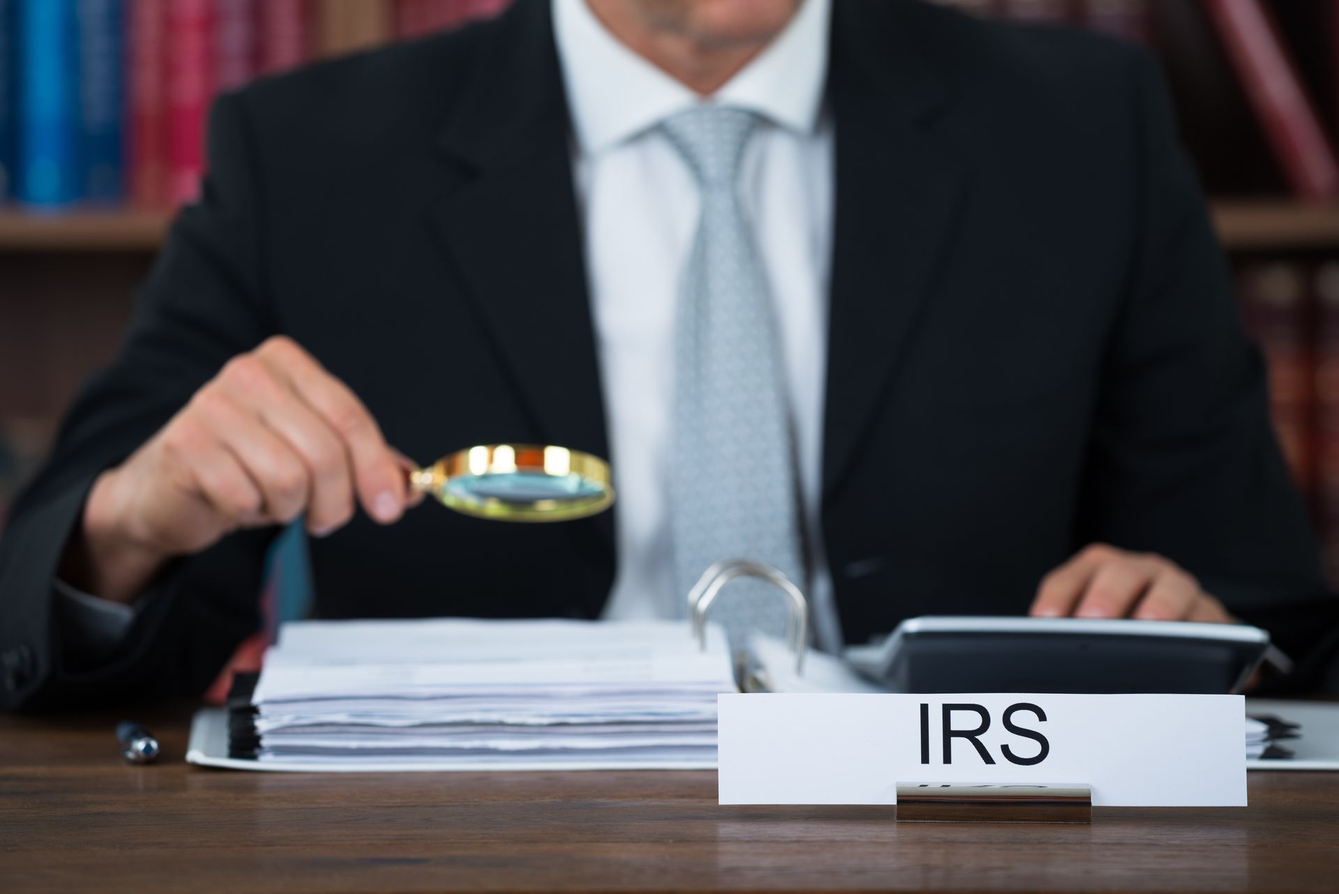 Person in suit holds magnifying glass over IRS paperwork.