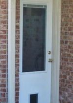 White door with a window and a pet door, set in a brick frame.