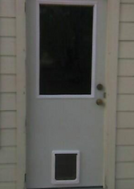 Gray door with a rectangular window and a dog door, set in a light-colored siding wall.