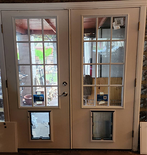Two cream-colored French doors with pet doors; one open, reflecting a porch and yard.