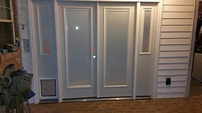 Double doors with sidelight, light grey with white trim. Pet door on the left. Siding on the right.
