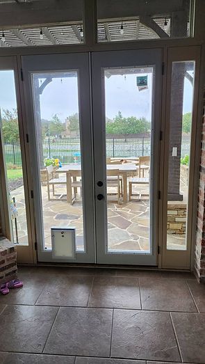 Glass double doors with a pet door opening to a patio with tables and a lawn.