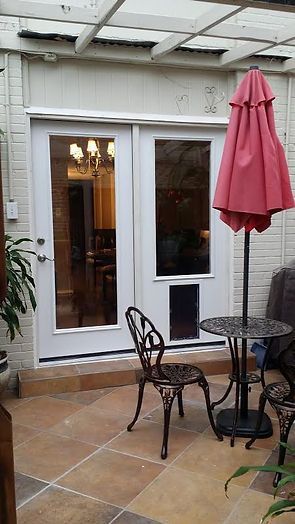 White French doors with dog door, red patio umbrella, patio furniture on tiled patio.
