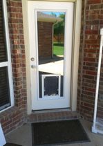 White door with dog door, set in brick wall, with a mat.