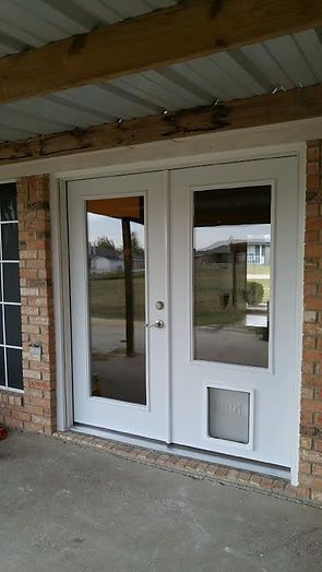 White double door with glass panels and a dog door, set in a brick building under a covered patio.