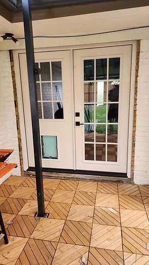 White French doors with dog door, on a wooden tile patio. A black pole is in the foreground.