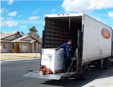 A worker loading a large box onto a truck using a pallet jack in a residential street.