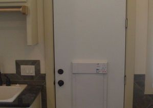 White door with alarm panel, dark hardware, in a room with a countertop and sink.