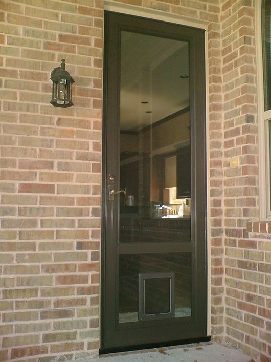 Brown screen door with cat door set in brick wall with lantern.