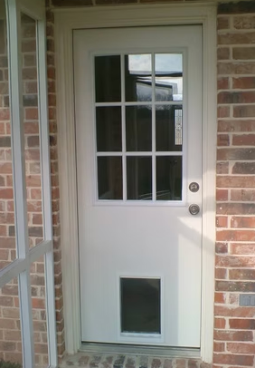 White exterior door with window panes, dog door, on a brick building.