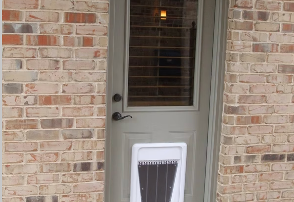 Brick wall with a gray door containing a dog door.