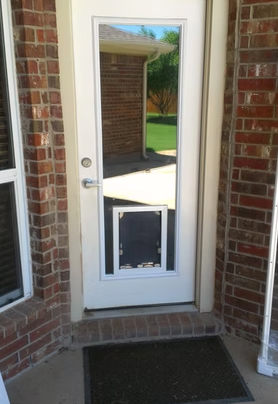 White door with dog door, brick exterior, and a mat.