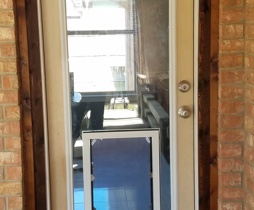 Glass door with dog door insert, framed by brick, with a view of an outdoor porch.