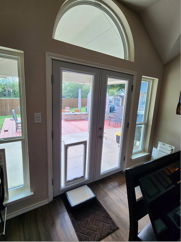 Interior view of double glass doors with a doggy door, leading to a backyard patio.