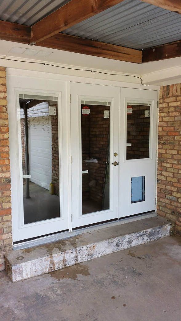 White French doors with a pet door, brick exterior, concrete step, and corrugated metal roof.