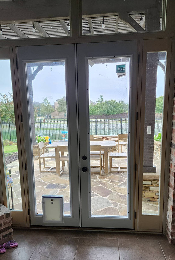 French doors with a pet door lead to a patio with furniture, under a cloudy sky.