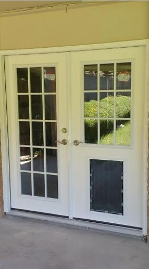 White double doors with a dog door, windows, and silver handles, set against a beige building.