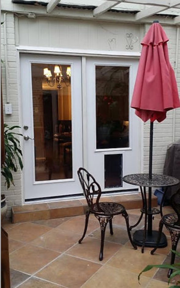 Patio doors with a built-in dog door, table, chairs, and a closed red umbrella.