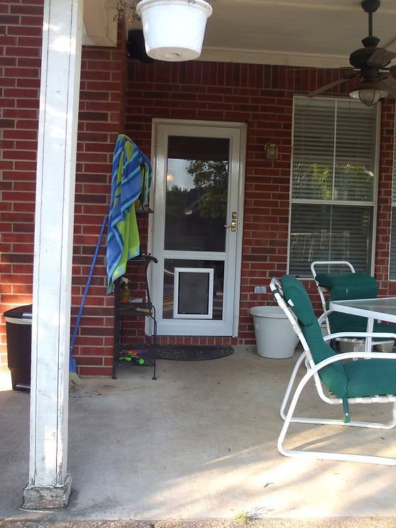 Brick porch with a white-framed screen door containing a pet door. A towel is hanging nearby.