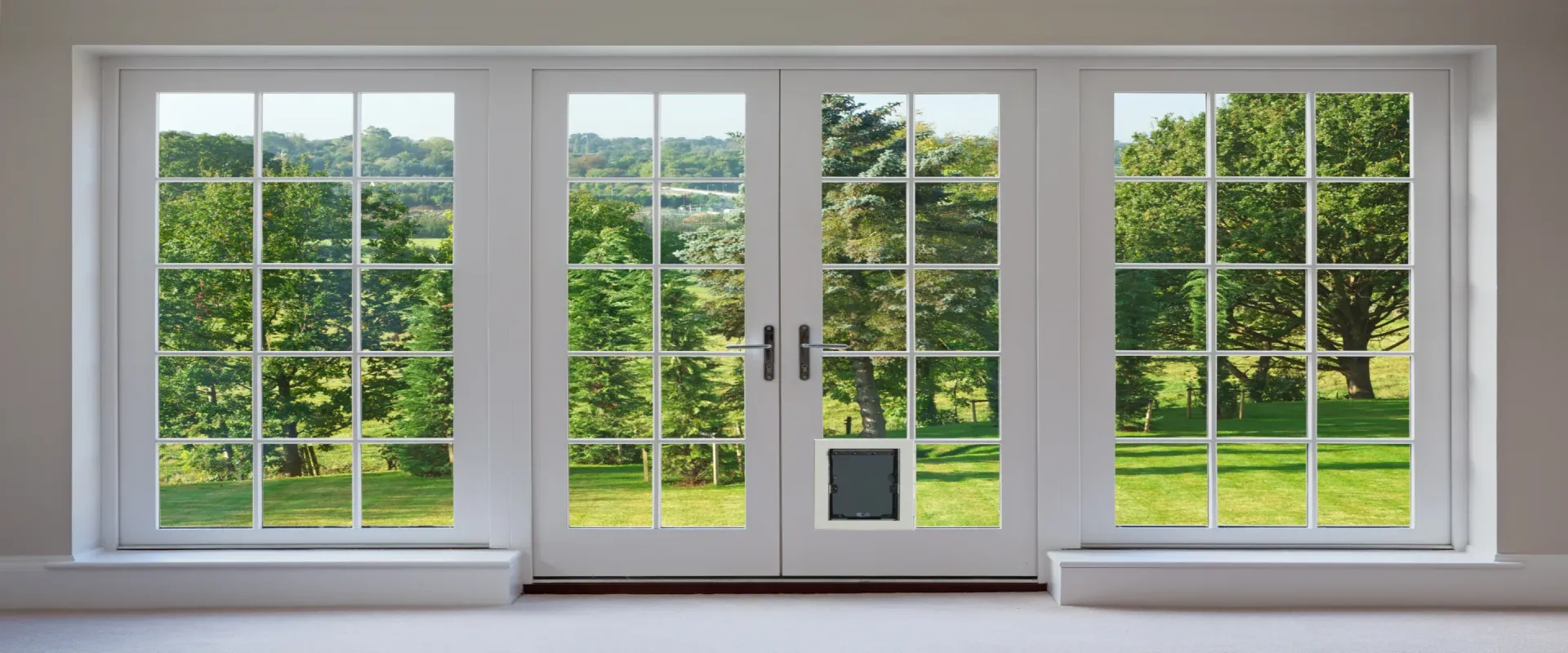 White French doors with multiple panes and a built-in pet door open to a green outdoor landscape.